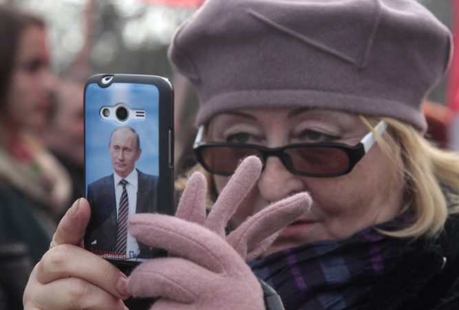 A portrait of Russian President Vladimir Putin is seen on a cover of a woman's phone as she takes pictures during celebrations of the Russian national holiday - Defender of the Fatherland Day in Sevastopol, Crimea, February 23, 2016. REUTERS/Pavel Rebrov       TPX IMAGES OF THE DAY      - RTX286Y8